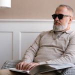 Senior man with sunglasses reading a braille book in a cozy modern interior.